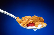 A spoonful of breakfast cereal of the corn-flake type, with milk and strawberry.