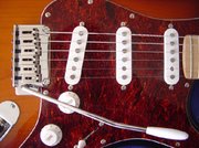 Detail of a Squier Stratocaster. Note the tremolo arm, the 3 single-coil pickups, the volume and tone knobs.