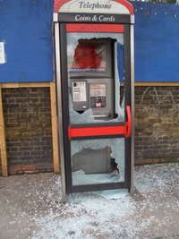 A vandalized phone booth with tempered glass