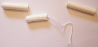 The elements of a tampon with applicator.  Left: the bigger tube ("penetrator")  Center: cotton tampon with attached string.  Right: the narrower tube.
