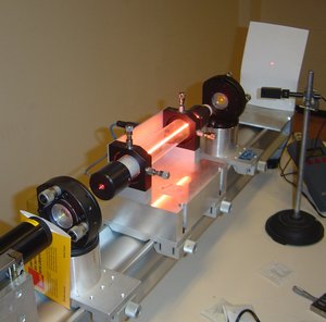 A  laser demonstration at the  at . The glowing ray in the middle is a electric discharge producing light in much the same way as a neon light; though it is the  through which the laser passes, it is not the laser beam itself which is visible there. The laser beam crosses the air and marks a red point on the screen to the right.